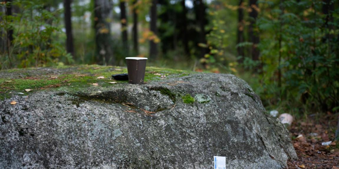 Muovinen kahvimuki kivenpäällä puistossa. Lääkeliuska kiven juurella.